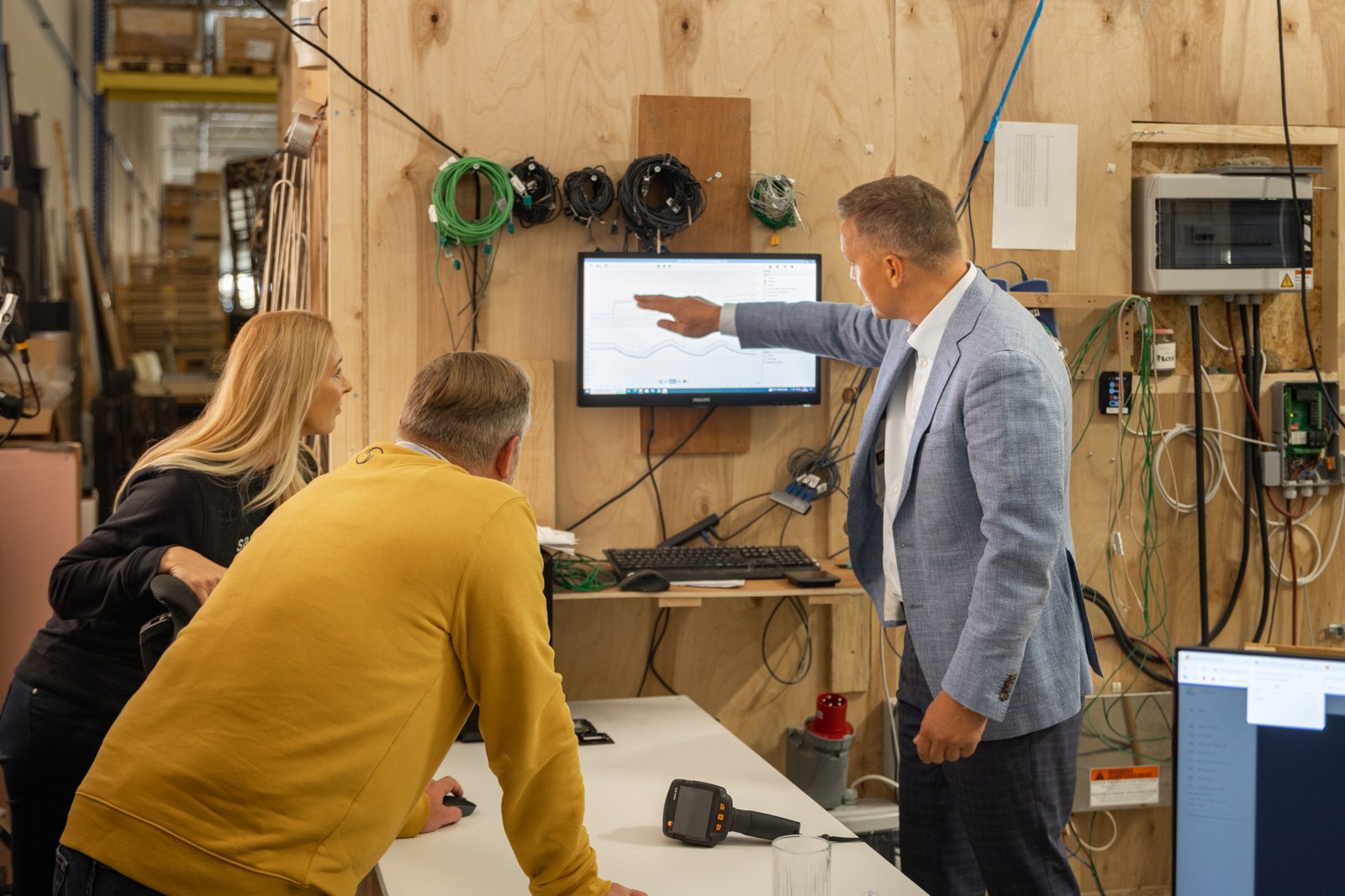 Saunum Test Lab In Tallinn With Sensor Wiring On A Plywood Wall And A Live Temperature Graph On The Screen